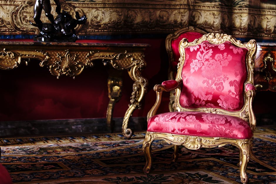 A luxurious bedroom in a historic home featuring a four-poster bed with a pink canopy and draped fabric, a wooden headboard, and matching side tables. The room has a red carpet, cream-colored walls ad