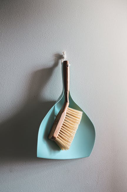 Two professional cleaning specialists from Brentford Carpet Cleaners stand back-to-back in a well-lit, minimalistic room with a plain white wall. One holds a carpet cleaner, and the other is holding a